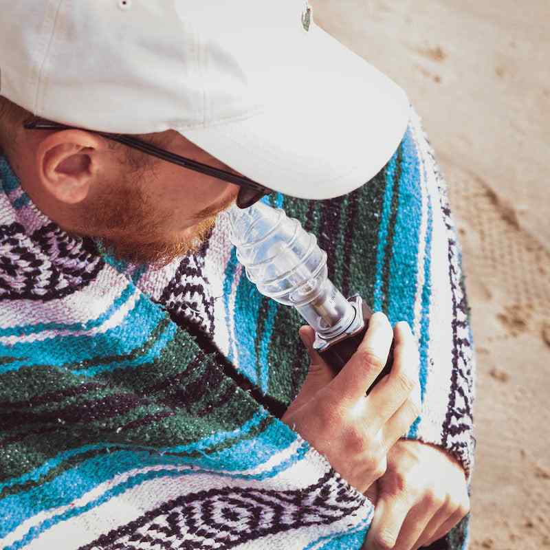 Linx Apollo Electric Dab Rig and E Nail in Portable Dab Rig mode with Linx Bubbler in use by a man wearing a hat, with a blue blanket wrapped around his shoulders.